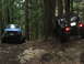 1990 Ford Bronco - Two modified off-road vehicles navigate a challenging trail through a dense forest.