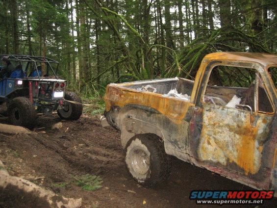 Burnt pickup truck on a muddy trail with an off-road buggy behind it in a forest