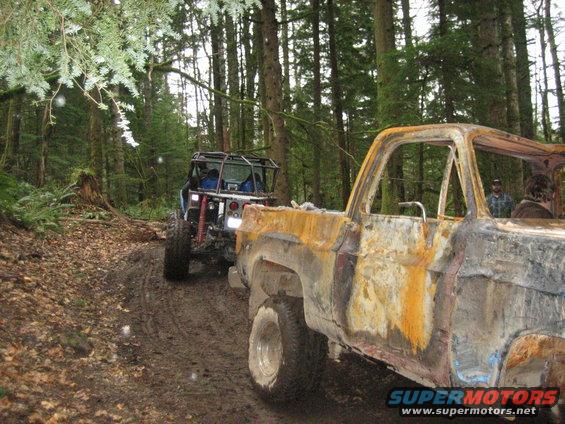 Burnt-out pickup truck and off-road vehicle on muddy forest trail