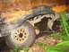 1990 Ford Bronco - Close-up of a heavily damaged vehicle's rear wheel well and suspension, showing rust and mud.