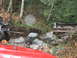1990 Ford Bronco - An off-road vehicle tows a stuck pickup truck out of a rocky, wooded area.