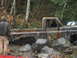 1990 Ford Bronco - A heavily damaged pickup truck sits in a wooded area, with a person observing it.