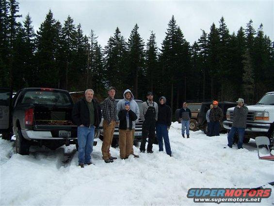 Group of people standing in snow next to several trucks and SUVs