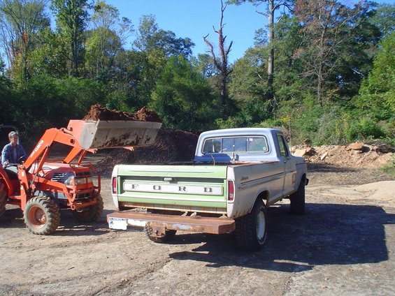 Ford pickup truck with green tailgate, rusty bumper, and lifted suspension