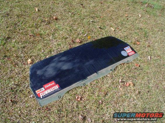 Tailgate glass with Edelbrock Flowmaster and MSD stickers on it, lying on grass