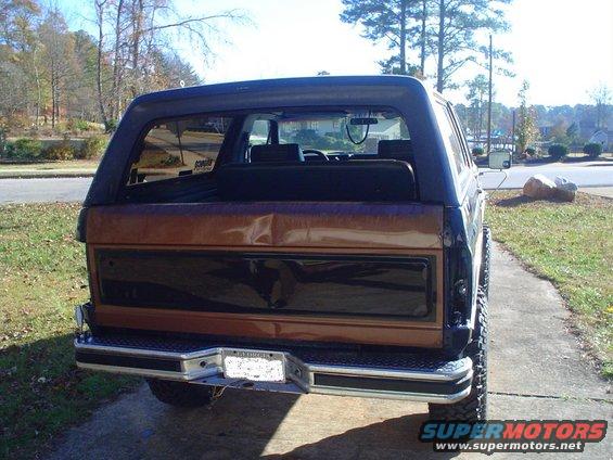 Rear view of a Ford Bronco with a brown and black tailgate, chrome bumper, and license plate. The vehicle appears to be from the early 1980s