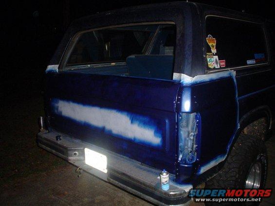 Rear of a dark blue SUV with masking tape around the tailgate and rear quarter panel, showing primer or body filler in a horizontal stripe