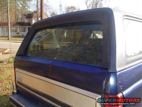 Rear of a blue and tan 1984 Ford Bronco with a dented tailgate