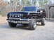 1989 Ford Bronco - This black Ford Bronco is parked on a gravel driveway with trees in the background.