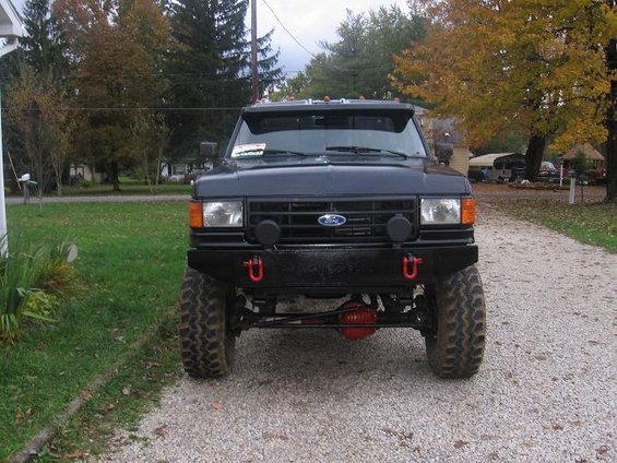 Front view of a black Ford F-Series truck with a custom bumper and red tow hooks. The grille has a Ford emblem