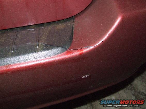 Red vehicle body panel with a crack and red paint chips near a black plastic trim piece