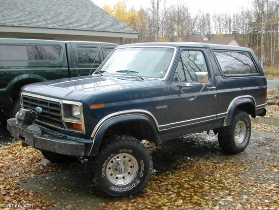 Dark blue Ford Bronco parked next to a green pickup truck. Bronco has a winch on the front bumper