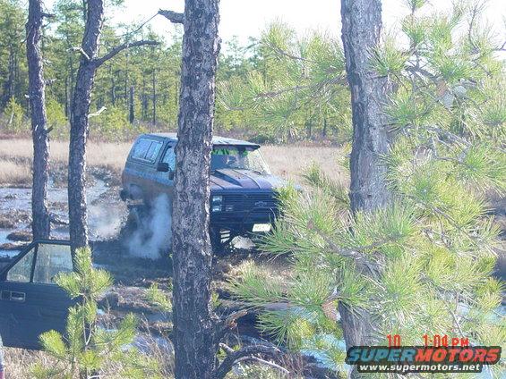 Dark blue SUV with aftermarket hood scoop stuck in mud, front passenger door open