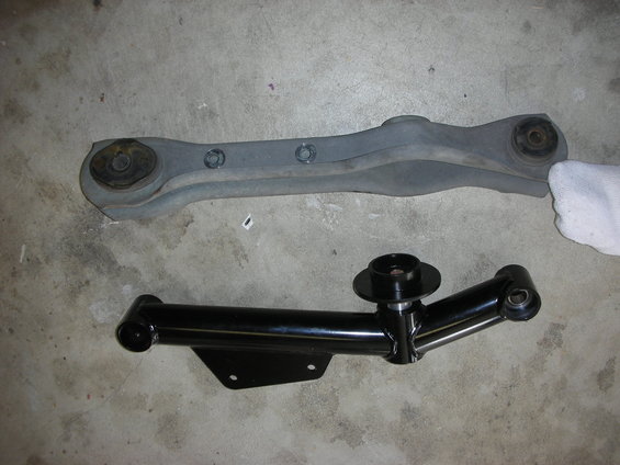 Two car suspension control arms, one gray and one black, on a concrete floor