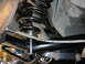 1990 Ford Mustang - The underside of a vehicle shows its rear suspension system, including a coil spring and various metal linkages.