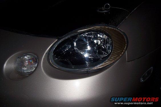 Close-up of a cracked headlight and fog light on a car. Hood has carbon fiber accents