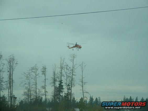 Orange helicopter flying over trees with a cable hanging down