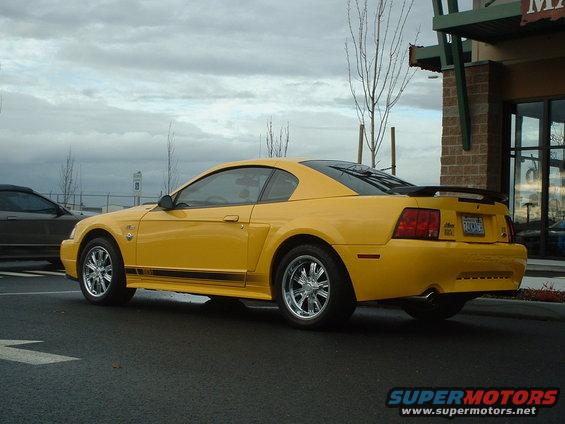 Yellow Ford Mustang coupe with black stripe and spoiler, parked next to a building
