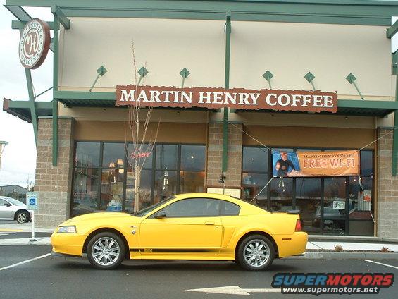 Yellow 2000 Ford Mustang parked outside Martin Henry Coffee shop. Side view