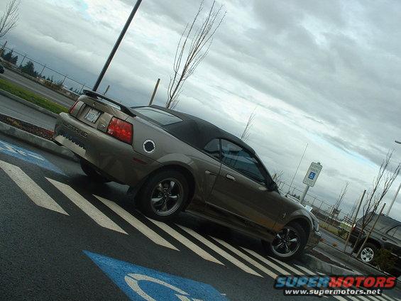 Brown convertible Mustang parked in a handicapped spot. Another SUV is parked nearby