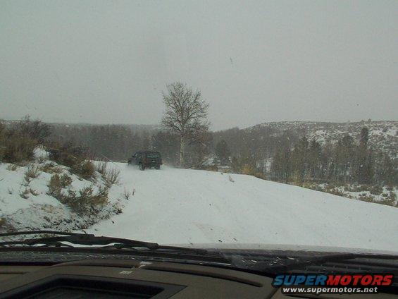 Dark SUV driving on a snow-covered road with trees and hills in the background