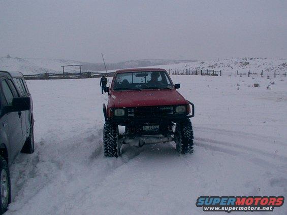 red Toyota pickup with big tires driving in snow, another SUV next to it
