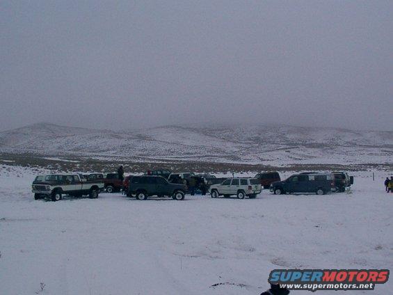 Several SUVs and trucks parked in a snowy field under a cloudy sky