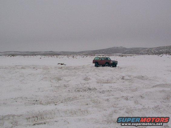 Red SUV with white top being towed in a snow-covered field under an overcast sky