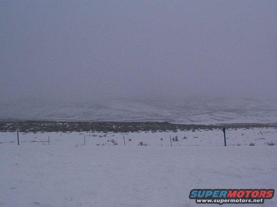 Snowy landscape with fence posts and distant hills under a hazy sky