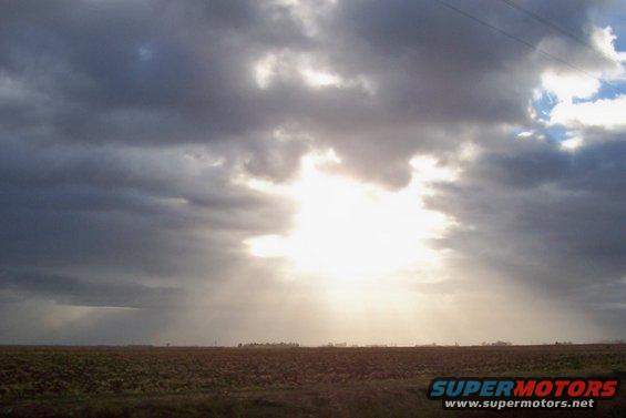 Overcast sky with sunbeams breaking through, over a flat, brown field