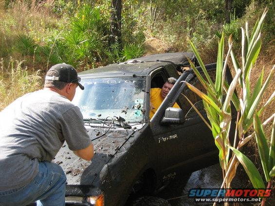 Black off-road vehicle stuck in mud, driver in yellow shirt visible