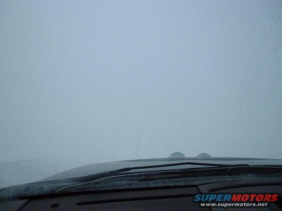 view from inside vehicle looking out windshield, dashboard visible, heavy fog outside
