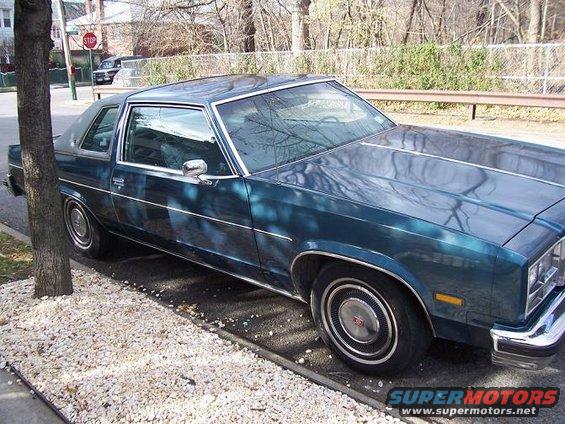 Dark teal coupe, 3/4 front view. Appears to be a 1977 Oldsmobile Cutlass Supreme