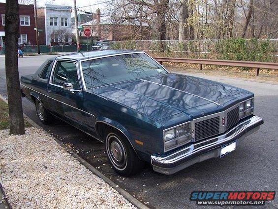 1977 Oldsmobile Cutlass Supreme coupe parked on street, dark teal paint, chrome trim