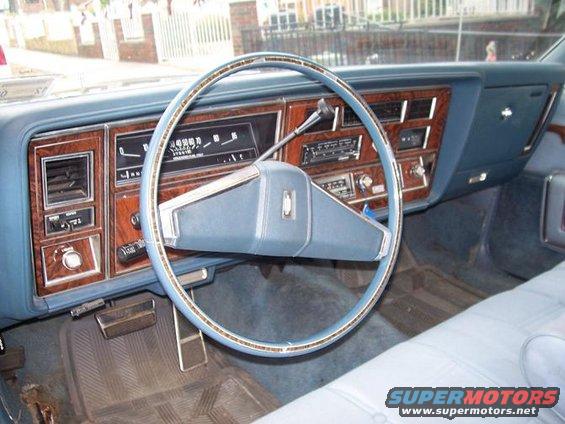 Car interior showing dashboard with wood grain trim, blue steering wheel, and instrument cluster