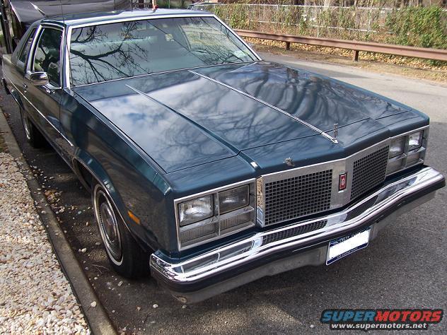 Teal Oldsmobile Cutlass Supreme coupe parked curbside. Chrome grille and bumper are prominent