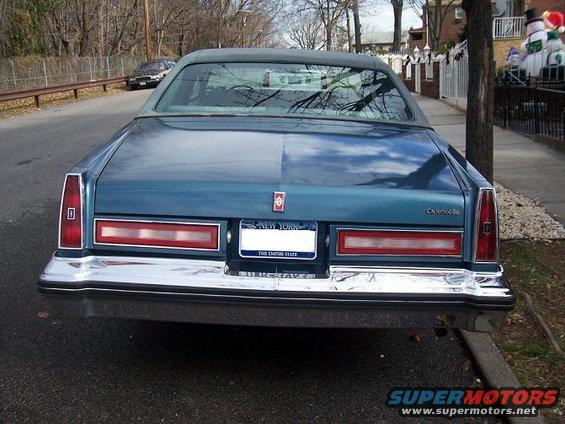 Blue sedan rear view, New York license plate, chrome bumper, parked on street