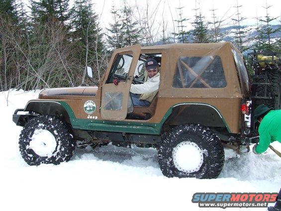Brown Jeep Wrangler with tan soft top stuck in snow, driver visible