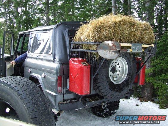 Bronco with spare tire, gas cans, shovel, axe, and hay on rear rack