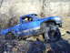 1994 Ford F-250 - A blue pickup truck is seen off-roading through a wooded area with uneven ground and obstacles.