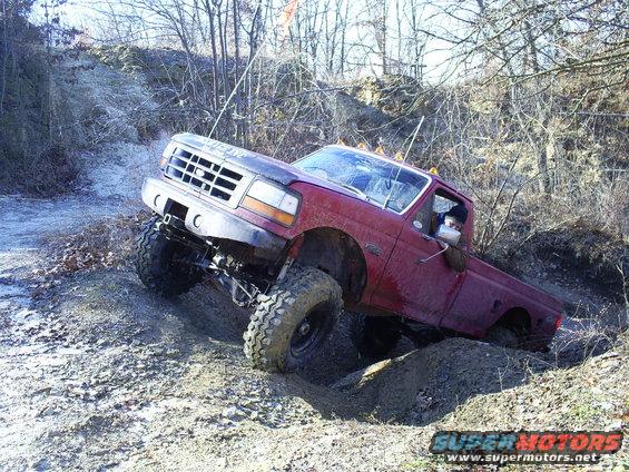 Red Ford F-series truck with large tires climbing a dirt hill