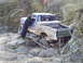 1994 Ford F-250 - A person checks on a pickup truck as it maneuvers over large rocks on a trail.