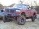 1994 Ford F-250 - A lifted red Ford pickup truck with large off-road tires is parked on a dirt surface, with another vehicle partially visible to the left.