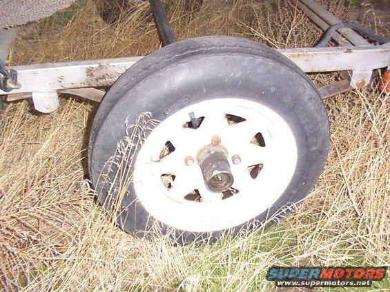 trailer wheel with white rim and black tire, sitting in dry grass