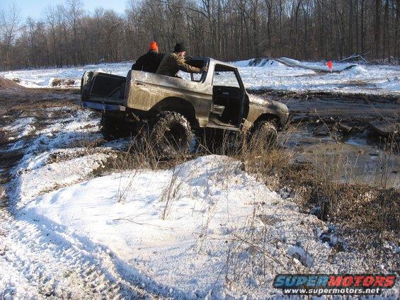 Ford Bronco with two people inside stuck in a muddy, snowy off-road area