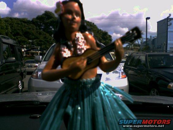Hula dancer figurine on dashboard with cars in background