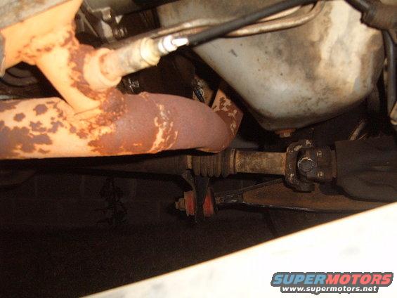 Underside view of rusty exhaust pipes and driveshaft with a Supermotors.net watermark