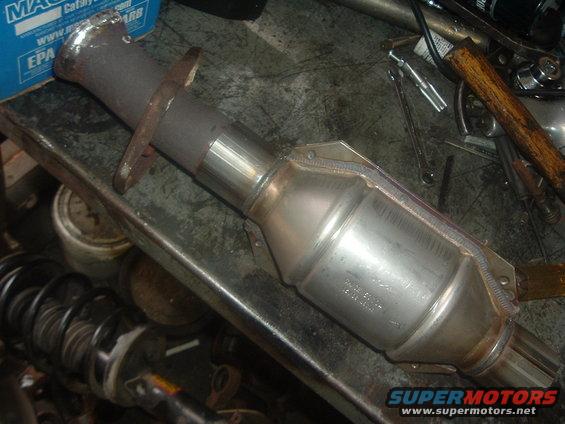 Catalytic converter with metal flanges on a workbench, tools and car parts in background