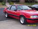 1990 Ford Mustang - A red 1990 Ford Mustang coupe is parked in front of a house, with another car visible behind it.