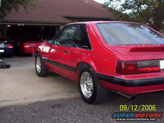 Red 1990 Ford Mustang hatchback parked in driveway, other cars visible in garage